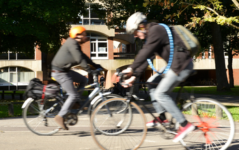 Two cyclists breezing through the Ƶ campus on a sunny day